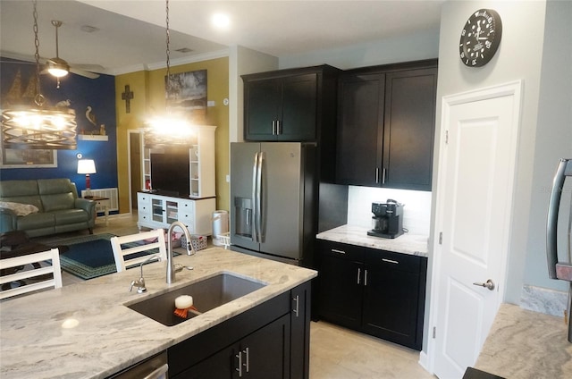 kitchen with a sink, decorative light fixtures, light stone counters, dark cabinetry, and stainless steel fridge