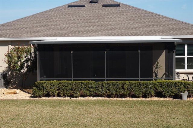 view of side of property with a lawn, roof with shingles, and a sunroom