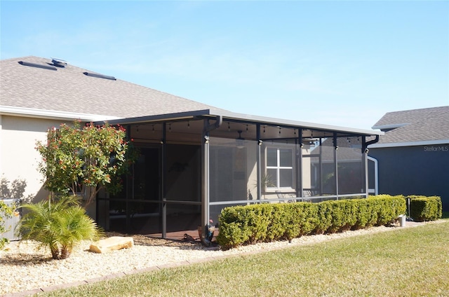 rear view of property with stucco siding, a lawn, a sunroom, and a shingled roof