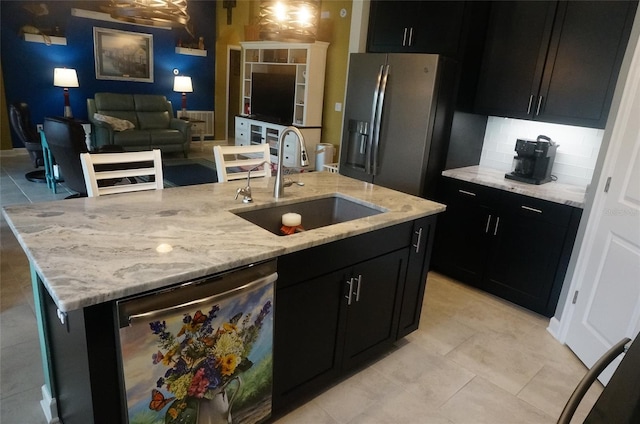 kitchen featuring an island with sink, a sink, open floor plan, stainless steel appliances, and dark cabinets