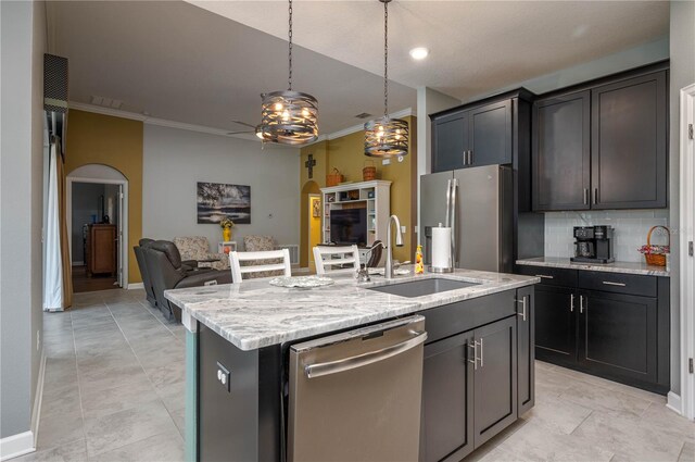 kitchen featuring light stone counters, a sink, stainless steel appliances, decorative backsplash, and ornamental molding