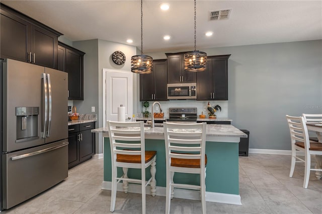 kitchen featuring pendant lighting, stainless steel appliances, a kitchen island with sink, baseboards, and visible vents
