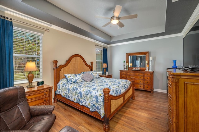 bedroom with baseboards, wood finished floors, ornamental molding, and a raised ceiling