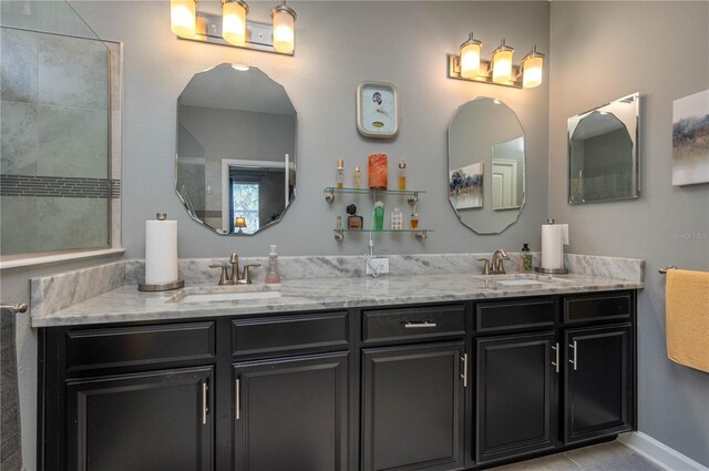 full bathroom with double vanity, tiled shower, baseboards, and a sink
