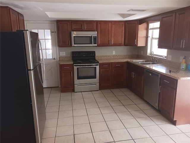 kitchen with appliances with stainless steel finishes, sink, light tile patterned floors, a tray ceiling, and light stone countertops