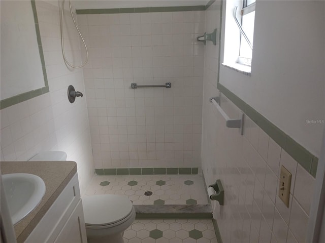 bathroom featuring vanity, a tile shower, tile walls, and toilet