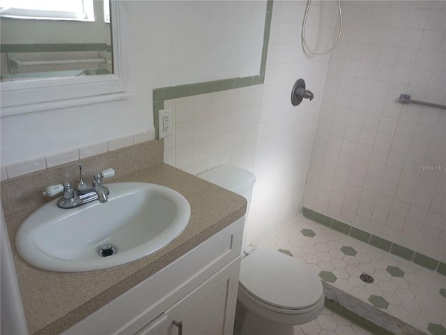 bathroom with tiled shower, vanity, toilet, and tile walls