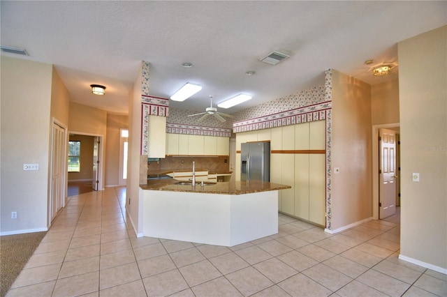 kitchen featuring sink, light tile patterned flooring, kitchen peninsula, and stainless steel refrigerator with ice dispenser