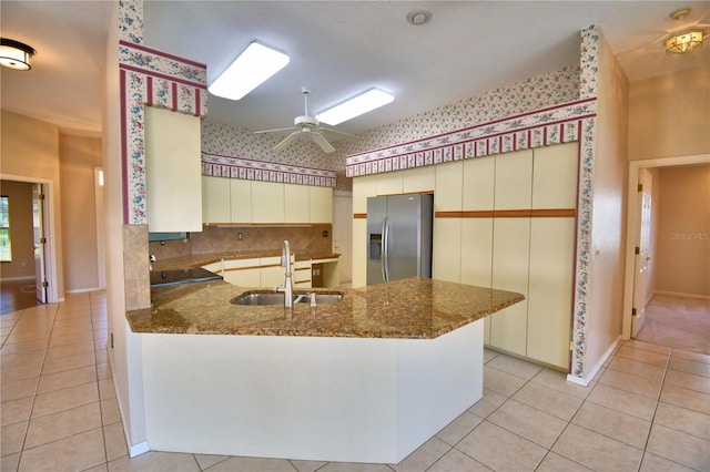 kitchen featuring sink, kitchen peninsula, stainless steel fridge with ice dispenser, and dark stone countertops