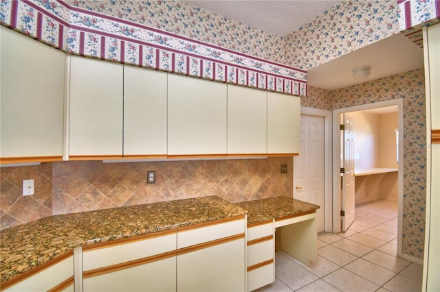 kitchen featuring dark stone countertops, built in desk, light tile patterned floors, and white cabinets