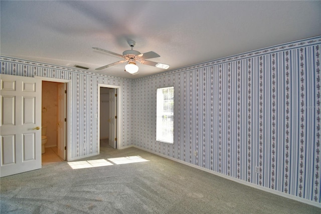 unfurnished bedroom featuring a spacious closet, light colored carpet, ceiling fan, ensuite bath, and a closet