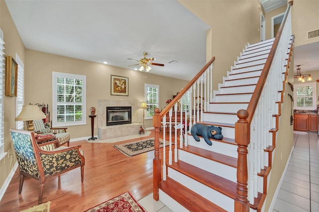 stairway featuring hardwood / wood-style flooring, ceiling fan, a premium fireplace, and a wealth of natural light