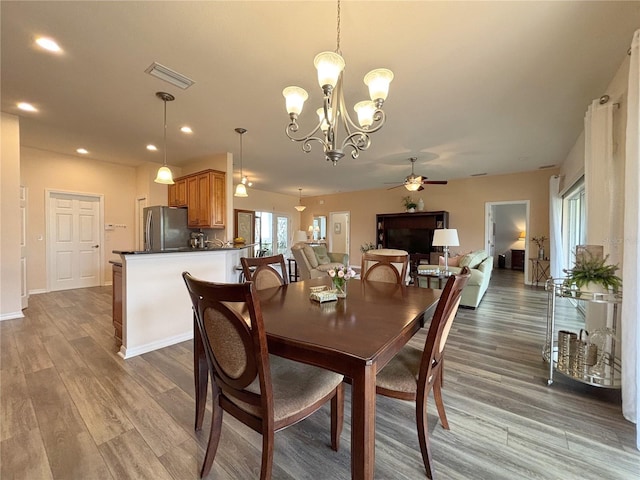 dining space with ceiling fan with notable chandelier and light hardwood / wood-style flooring