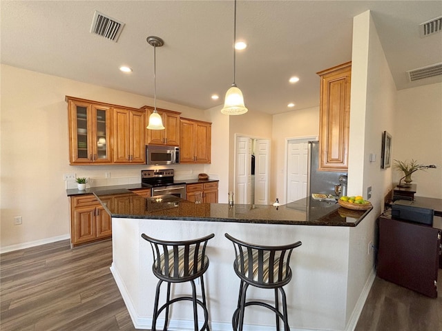 kitchen featuring pendant lighting, kitchen peninsula, dark stone counters, and appliances with stainless steel finishes