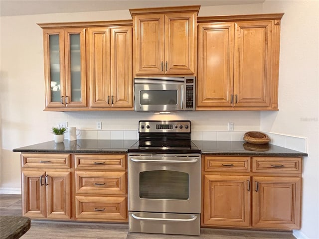 kitchen with stainless steel appliances, light wood-type flooring, and dark stone countertops