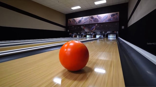 rec room with hardwood / wood-style flooring, a bowling alley, and a paneled ceiling