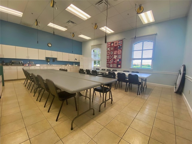 dining area with a towering ceiling, light tile patterned floors, and a drop ceiling