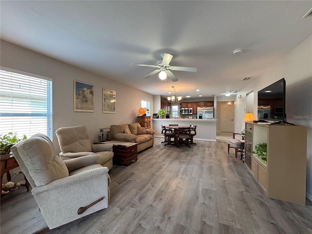 living room featuring ceiling fan with notable chandelier and light wood-type flooring