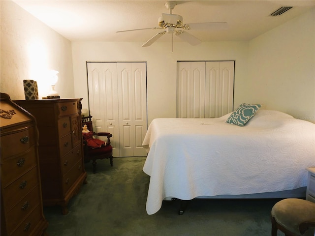 bedroom with ceiling fan, two closets, and dark colored carpet