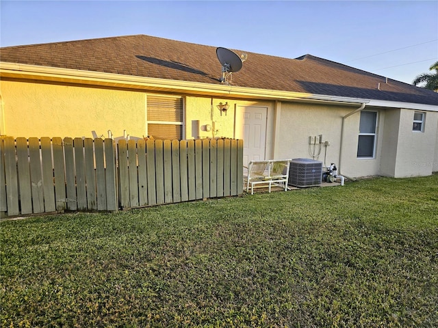 back of house with central AC unit and a lawn