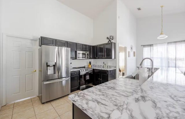 kitchen with light tile patterned flooring, appliances with stainless steel finishes, decorative light fixtures, sink, and a high ceiling