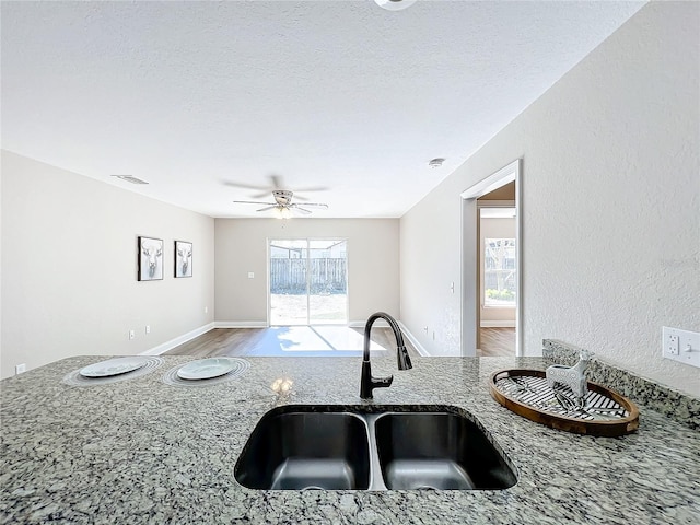 kitchen featuring stone countertops, wood-type flooring, sink, ceiling fan, and a textured ceiling