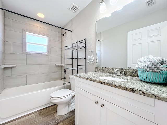 full bathroom with tiled shower / bath combo, vanity, hardwood / wood-style floors, and toilet