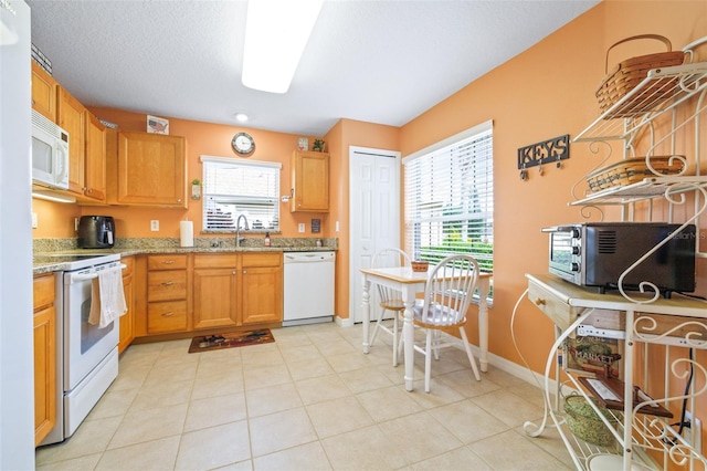 kitchen with light tile patterned flooring, sink, white appliances, light stone countertops, and a textured ceiling