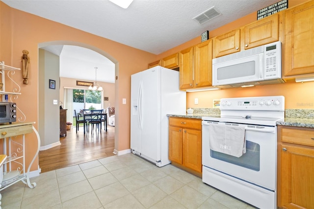 kitchen featuring an inviting chandelier, a textured ceiling, light tile patterned floors, white appliances, and light stone countertops