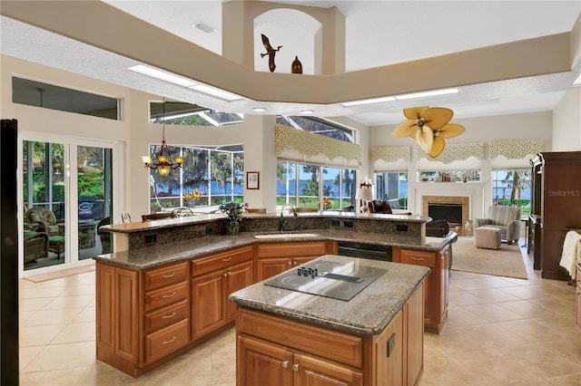 kitchen with sink, light tile patterned floors, a center island, black appliances, and a tiled fireplace