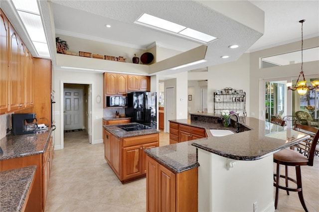 kitchen featuring a breakfast bar, decorative light fixtures, an island with sink, sink, and black appliances