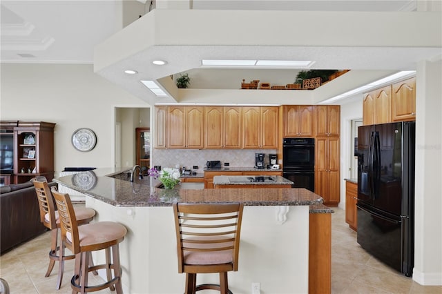 kitchen featuring backsplash, a kitchen breakfast bar, a large island with sink, ornamental molding, and black appliances