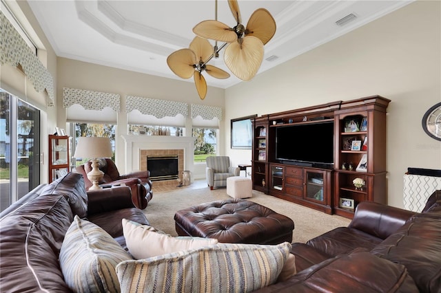 carpeted living room featuring ceiling fan, a towering ceiling, a tray ceiling, a fireplace, and ornamental molding