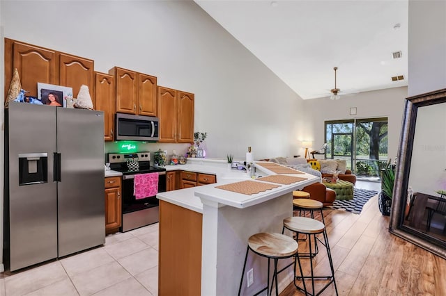 kitchen featuring appliances with stainless steel finishes, high vaulted ceiling, sink, a kitchen bar, and kitchen peninsula