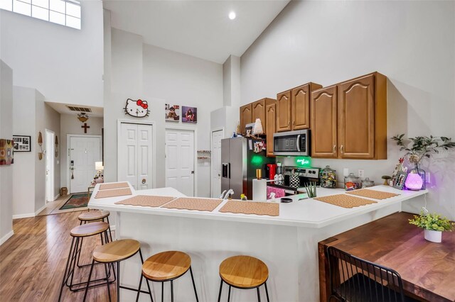 kitchen featuring light hardwood / wood-style flooring, high vaulted ceiling, stainless steel appliances, a kitchen bar, and kitchen peninsula