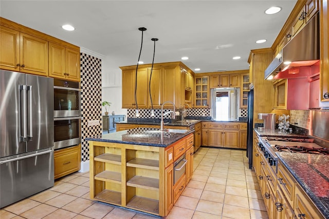 kitchen with pendant lighting, light tile patterned floors, stainless steel appliances, a center island with sink, and dark stone counters