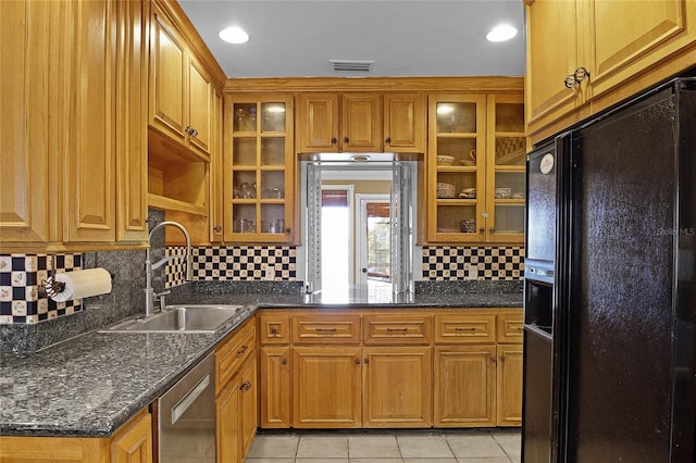 kitchen with sink, dark stone counters, stainless steel dishwasher, light tile patterned floors, and black refrigerator with ice dispenser