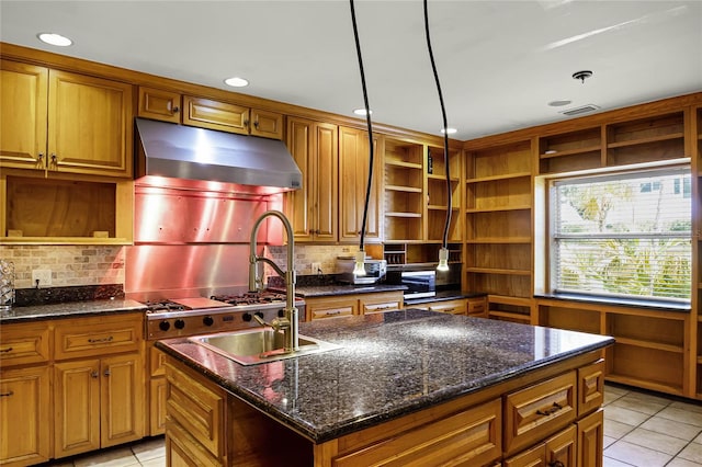 kitchen featuring pendant lighting, light tile patterned floors, an island with sink, exhaust hood, and dark stone counters