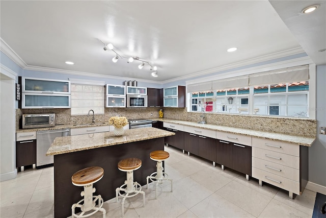 kitchen featuring backsplash, stainless steel appliances, dark brown cabinetry, light stone countertops, and a kitchen island
