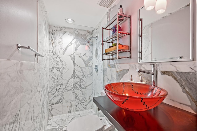 bathroom with sink, a tile shower, tile walls, and toilet