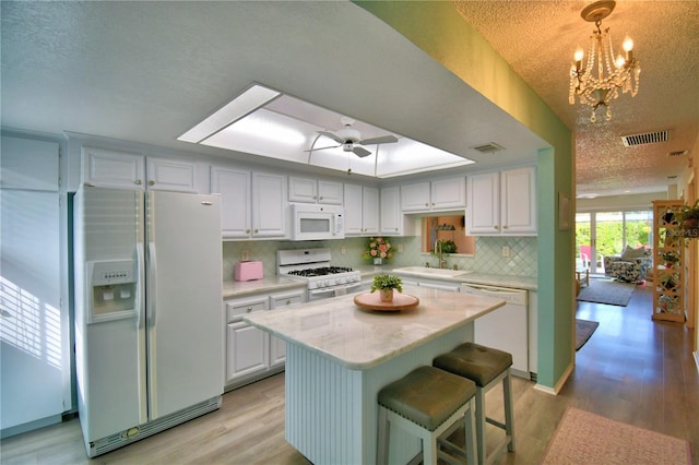 kitchen with a kitchen island, decorative light fixtures, sink, white cabinets, and white appliances