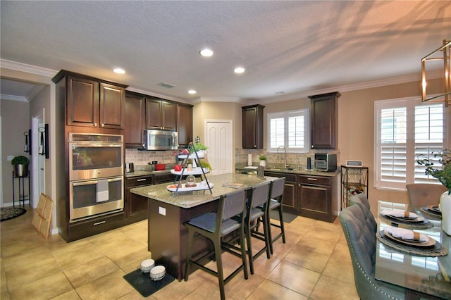 kitchen with crown molding, appliances with stainless steel finishes, dark brown cabinets, a center island, and light stone counters