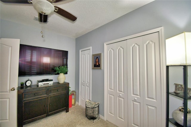 interior space featuring multiple closets, ceiling fan, light carpet, and a textured ceiling