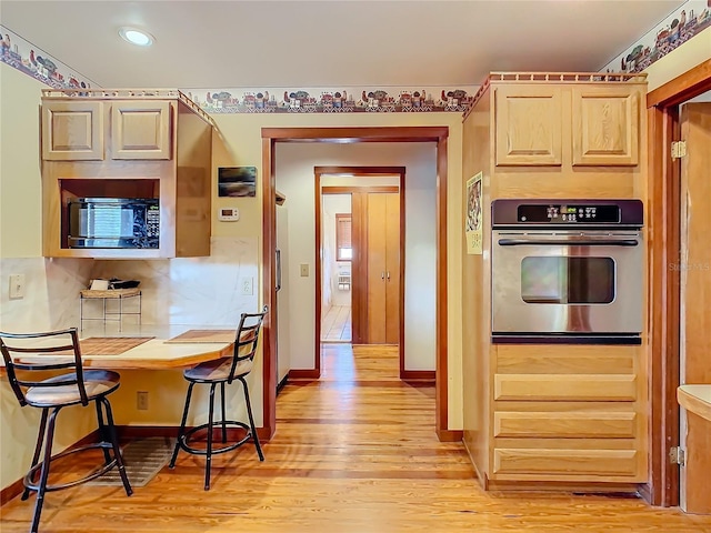 kitchen with light brown cabinets, stainless steel oven, and light wood-type flooring