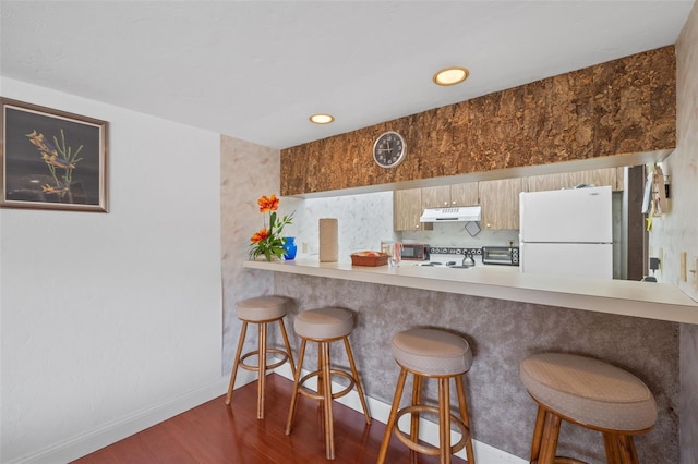 kitchen featuring dark hardwood / wood-style flooring, a kitchen breakfast bar, kitchen peninsula, and white refrigerator