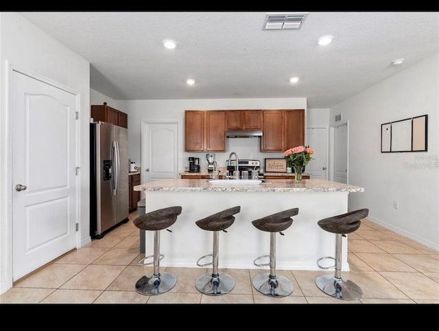 kitchen with sink, a kitchen bar, light tile patterned floors, stainless steel fridge with ice dispenser, and a center island with sink