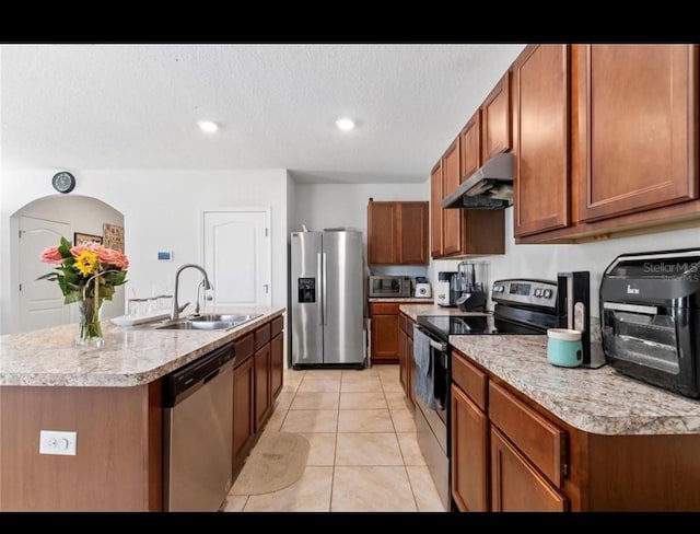 kitchen with sink, a textured ceiling, light tile patterned floors, appliances with stainless steel finishes, and a kitchen island with sink