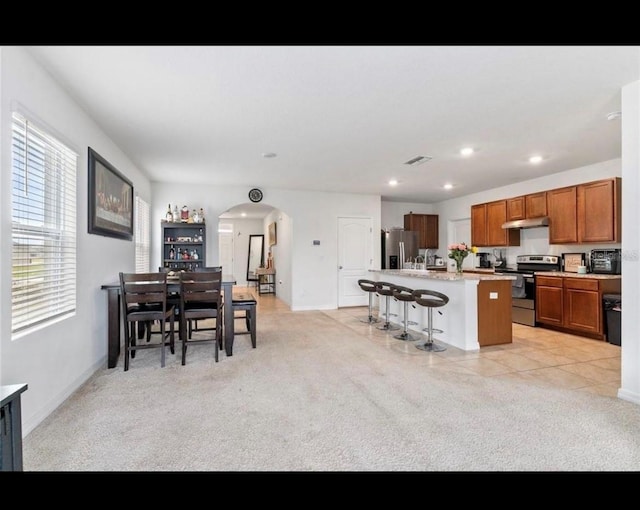 kitchen with light carpet, a breakfast bar, appliances with stainless steel finishes, and a center island with sink