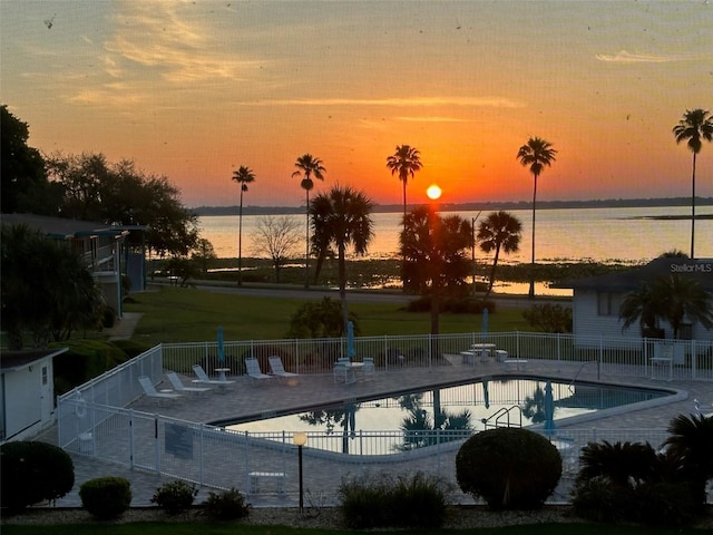 pool at dusk featuring a water view and a patio area