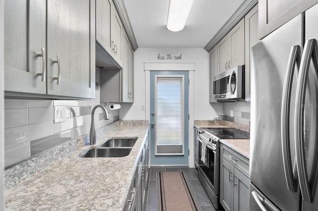 kitchen with stainless steel appliances, sink, light stone counters, and gray cabinets